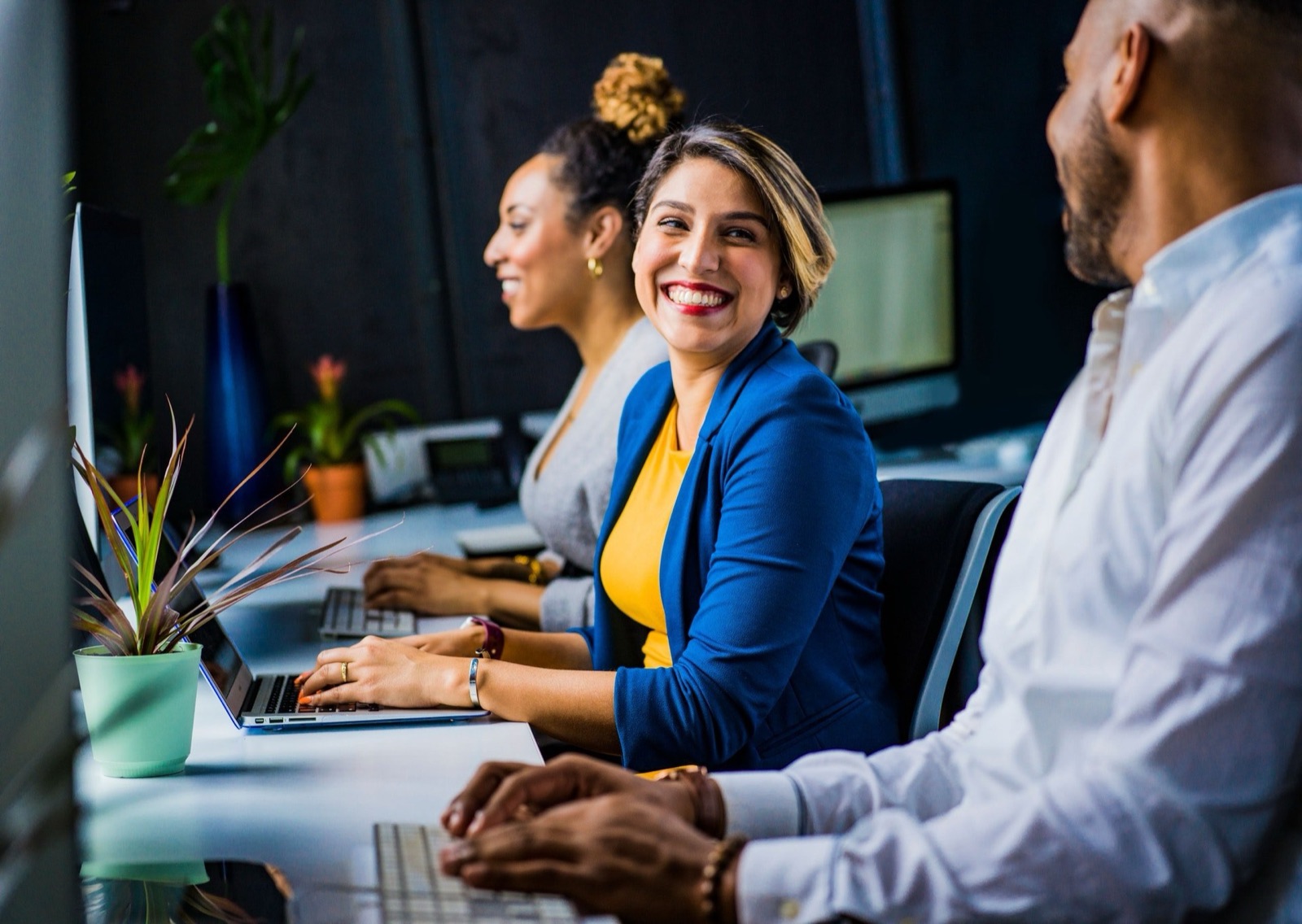 Three coworkers smiling together at a row of office computers