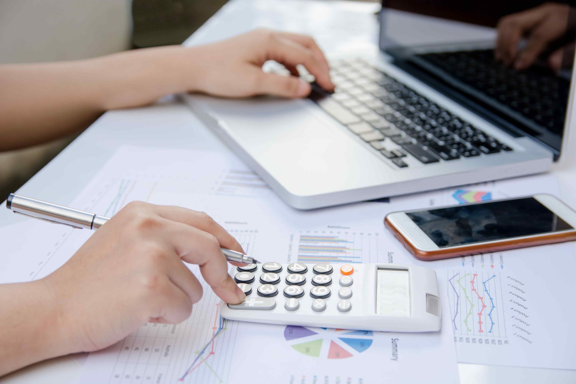 Accountant using a calculator and laptop while reviewing financial charts
